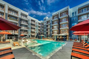 a swimming pool with chaise lounge chairs and umbrellas in front of an apartment building
